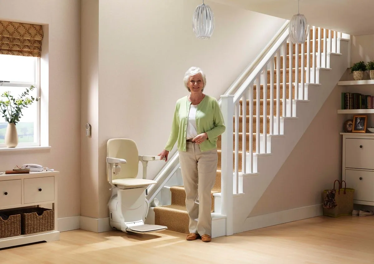 Une femme âgée se tient près du monte-escalier installé dans l’entrée de sa maison