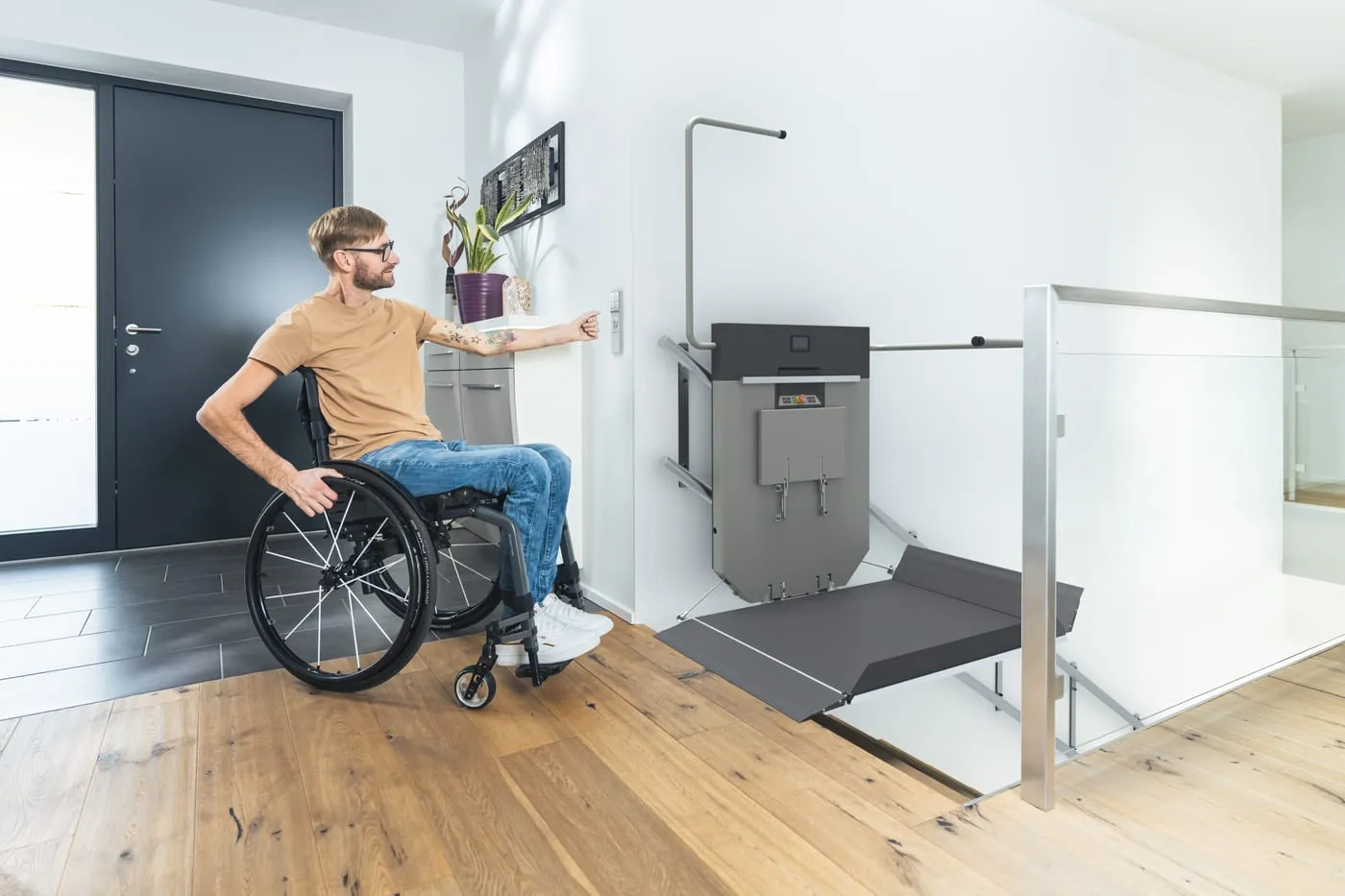 Un homme en fauteuil roulant appelle une plateforme élévatrice depuis le palier de sa maison