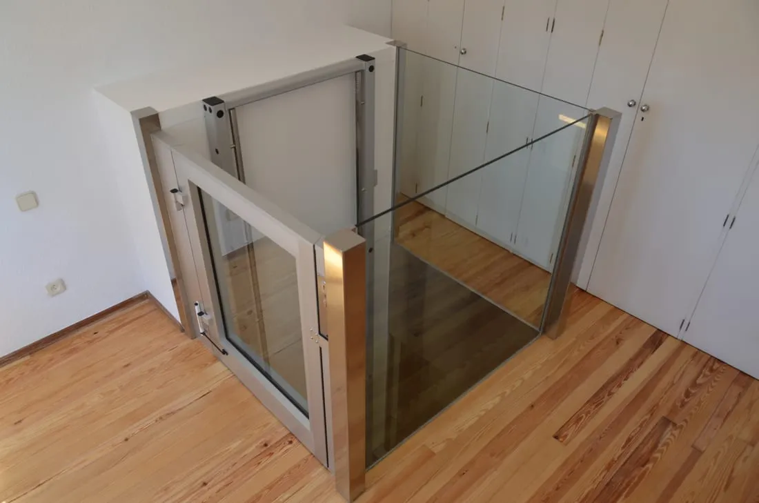Élévateur vertical vitré installé dans une maison, sur un parquet en bois